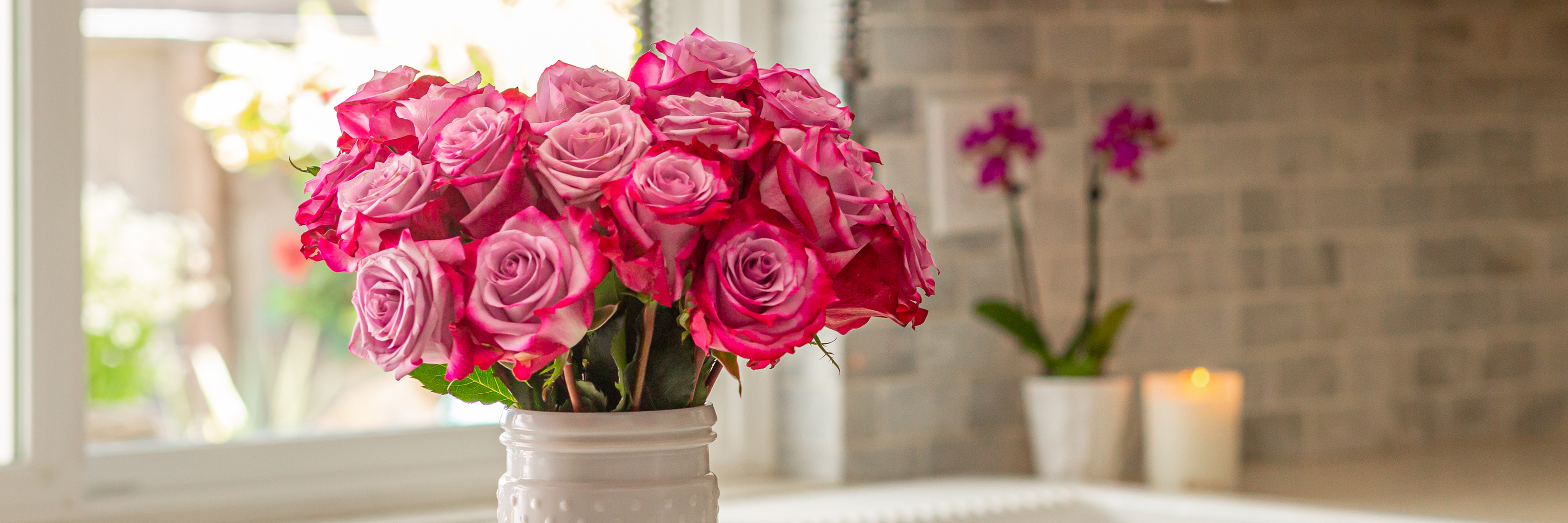 Vibrant pink roses elegantly arranged in a white vase, enhancing a bright kitchen setting.