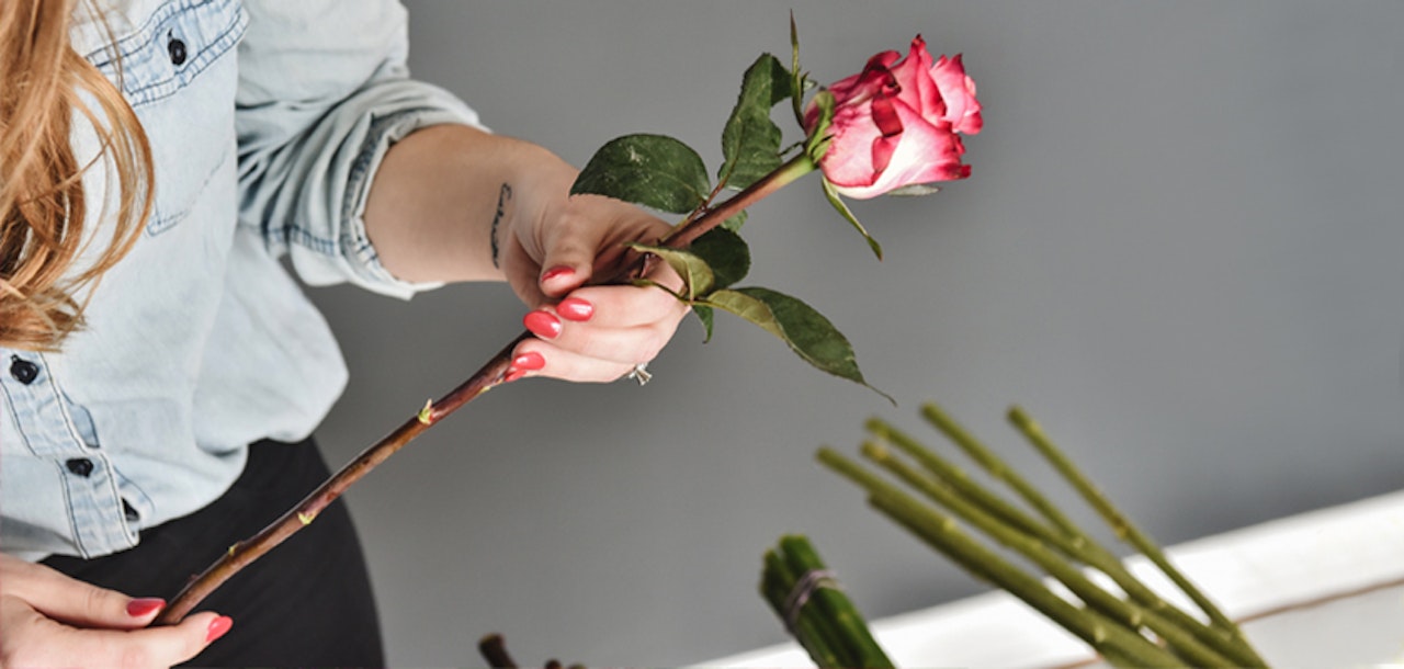 A woman holding a pink rose, preparing it for a floral arrangement, showcasing elegance.