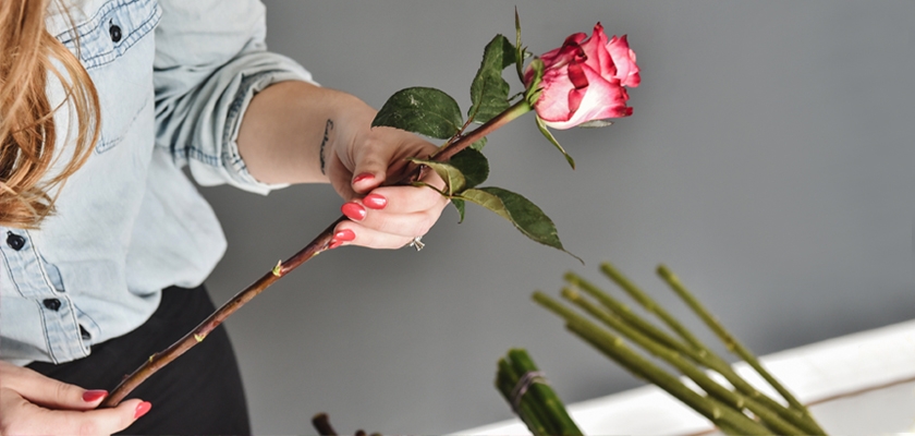 A woman holding a pink rose, preparing it for a floral arrangement, showcasing elegance.