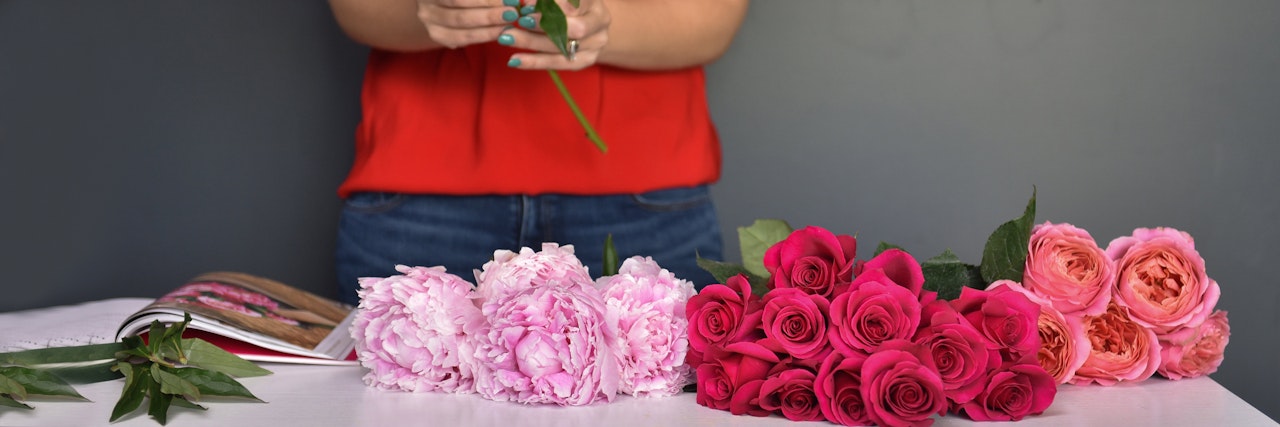 A florist designing a vibrant floral arrangement with pink and red roses and peonies.