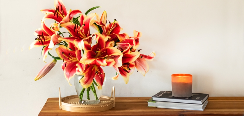 Vibrant bouquet of orange and yellow lilies beside a lit candle and books, enhancing home decor.
