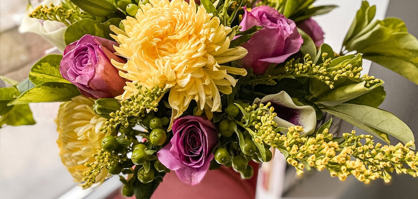Vibrant floral arrangement featuring yellow chrysanthemums, purple roses, and greenery.