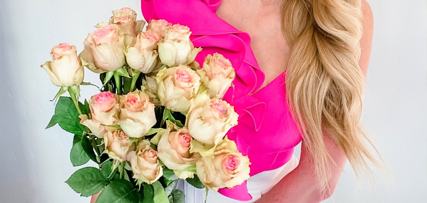 A woman holding a bouquet of pale pink and white roses with lush green leaves, perfect for gifting.