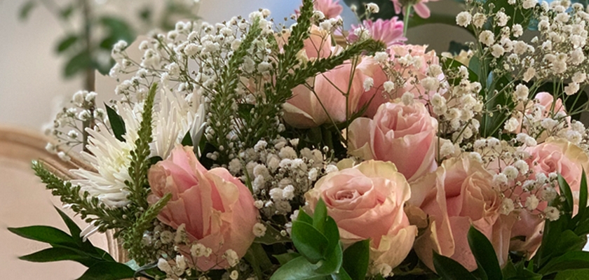 Delicate pink roses surrounded by greenery and white baby's breath in a charming floral arrangement.