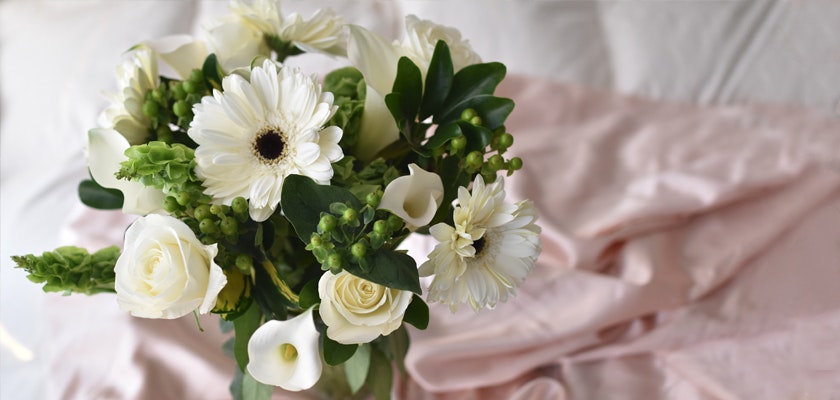 Elegant white floral bouquet featuring roses, gerbera daisies, and green accents on soft fabric.