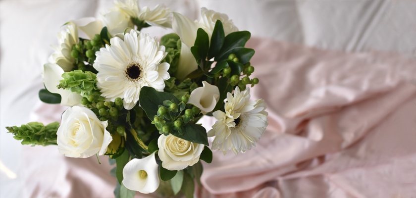 Elegant white floral bouquet featuring roses, gerbera daisies, and green accents on soft fabric.