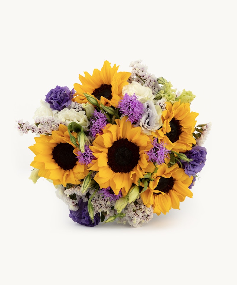 Beautiful bouquet of bright sunflowers, purple flowers, and mixed greenery arranged in a lush cluster, isolated on a white background.