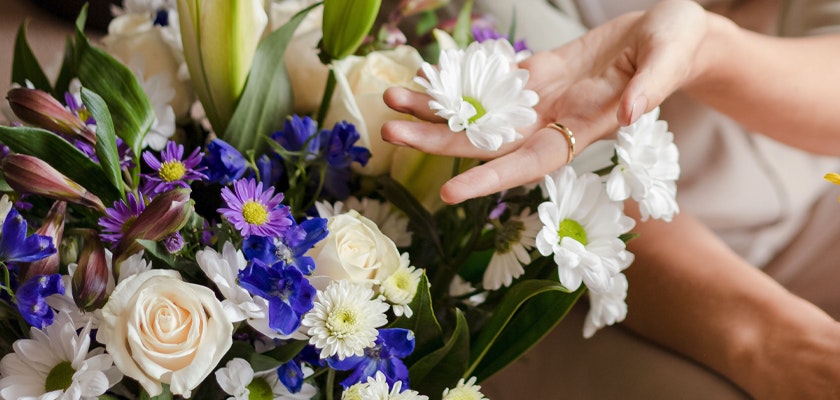 A vibrant floral arrangement featuring white daisies and colorful blooms, elegantly held by a hand.