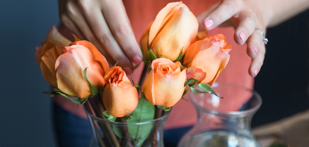 Delicate peach roses being arranged in a stylish glass vase by a careful florist.