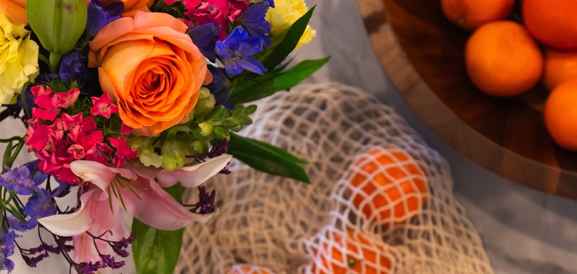 A vibrant floral arrangement with orange roses and colorful blooms beside fresh oranges.