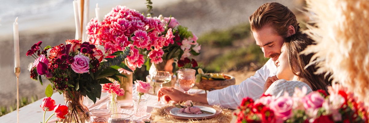 Intimate beachside dinner setup with vibrant floral arrangements and candles, perfect for couples.