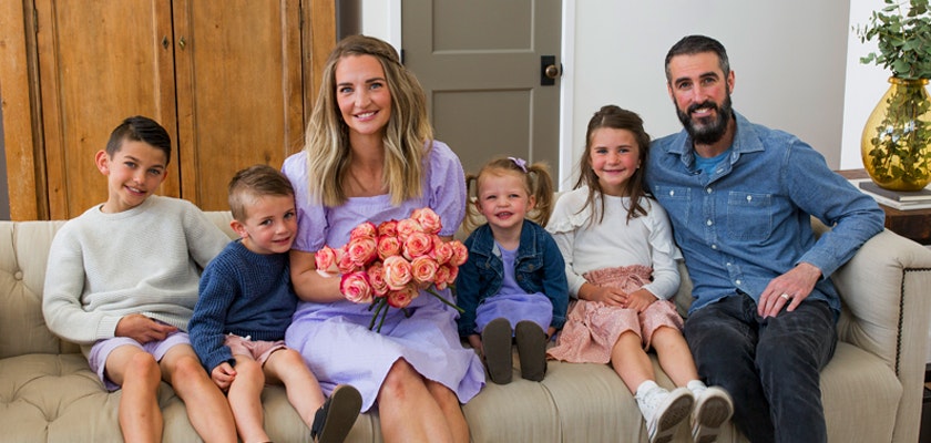A cheerful family of six posing together, surrounded by warmth and love, with a bouquet of roses.