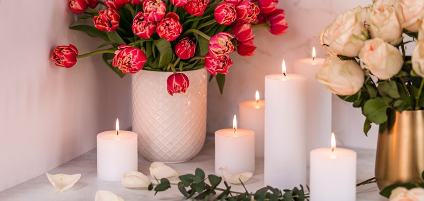 Elegant pink tulips in a vase surrounded by glowing candles and rose petals.