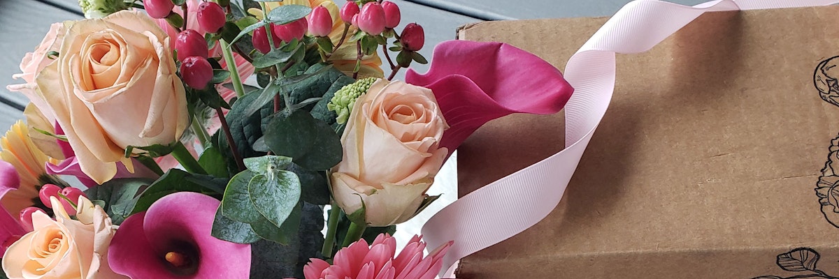 Charming floral arrangement with peach roses and vibrant blooms beside a gift box.