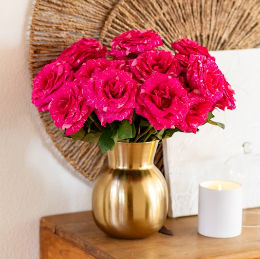 Vibrant pink roses in a chic gold vase, adding elegance to any room's decor.