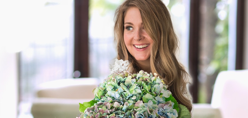 A joyful woman holding a lush bouquet of green and blue hydrangeas, showcasing vibrant blooms.