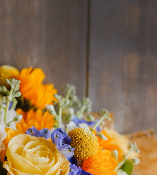 Vibrant floral arrangement featuring yellow roses, blue blooms, and seasonal greens.