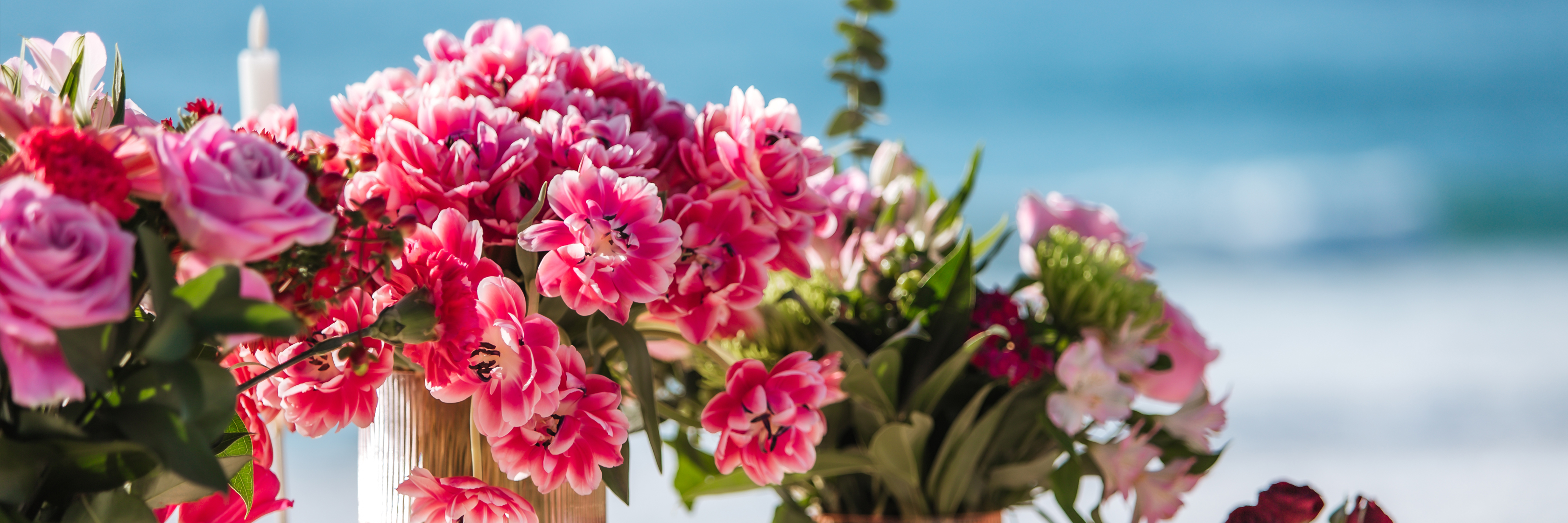 Vibrant floral arrangements featuring pink and red flowers by the beach, perfect for special events.