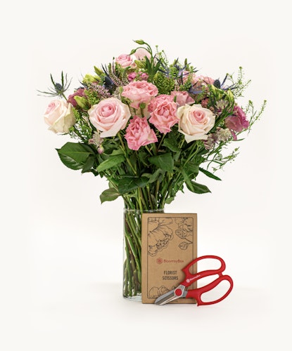 A lovely floral bouquet featuring pink and cream roses, complemented by greenery and scissors.