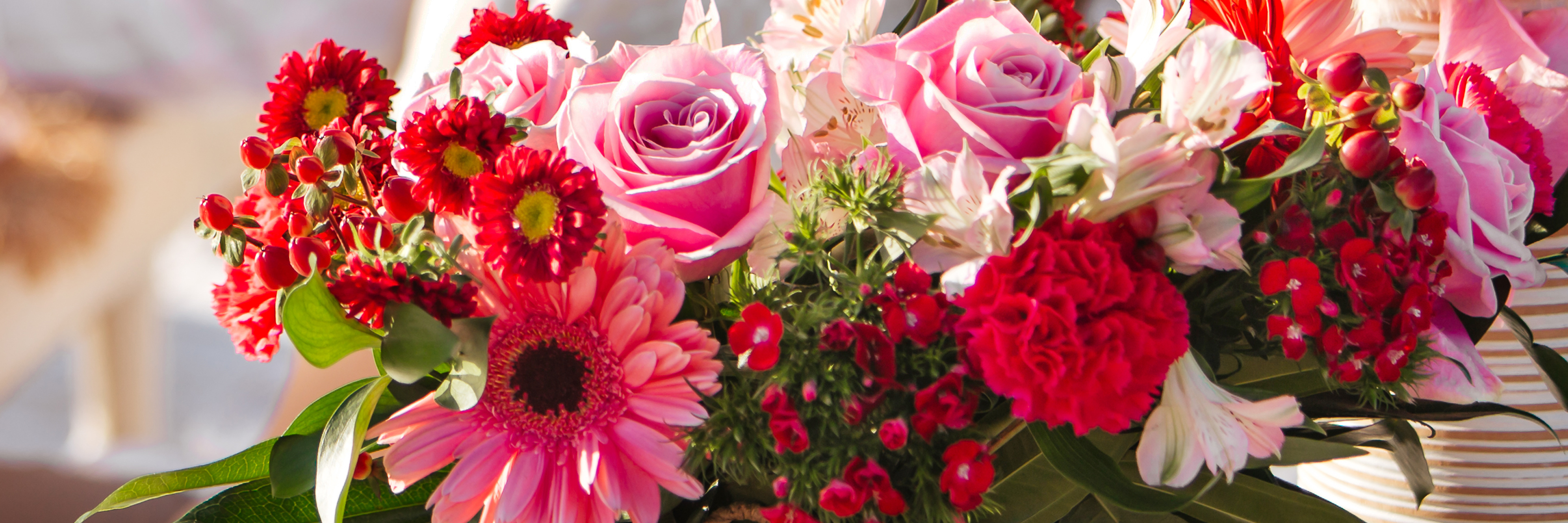 A vibrant floral arrangement featuring pink roses, red gerbera daisies, and assorted greenery.