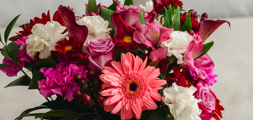 Vibrant mixed floral bouquet featuring pink gerbera daisies, roses, and deep red blooms.