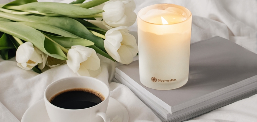 Cozy scene featuring white tulips, a lit candle, and a cup of coffee on a soft blanket and books.