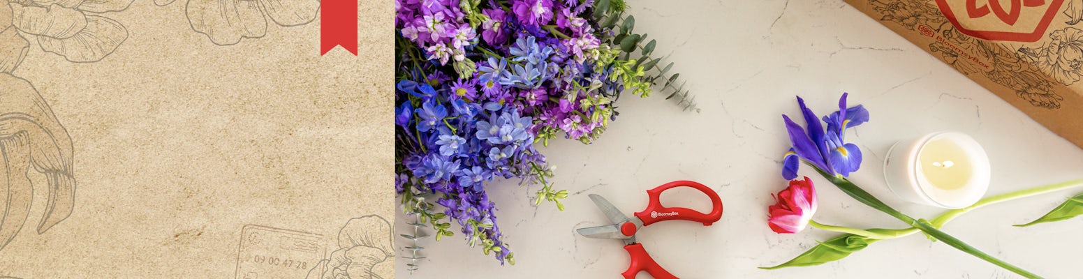 A vibrant assortment of blue and purple flowers with gardening scissors and a candle on a table.