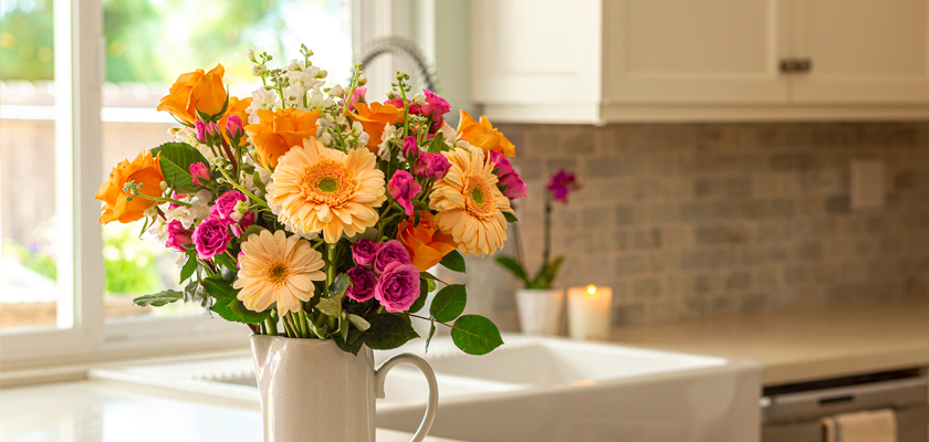 Vibrant floral arrangement featuring orange gerberas, pink roses, and cheerful blooms in a kitchen.