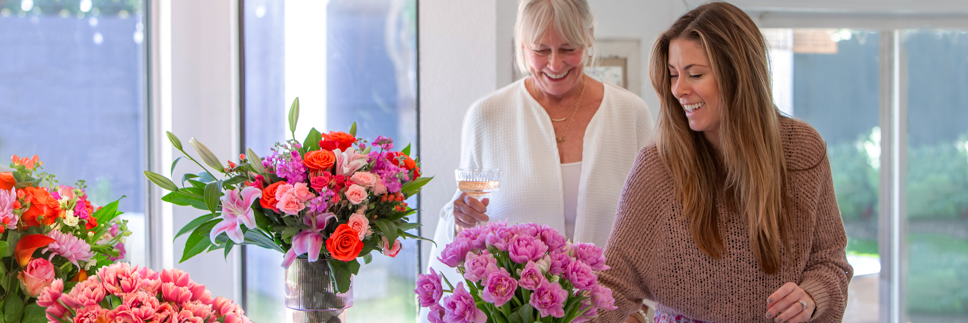 Two women joyfully arranging vibrant flower bouquets in a bright, welcoming space.