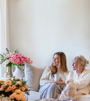 Two women enjoying a cozy moment together with tea, surrounded by beautiful floral arrangements.