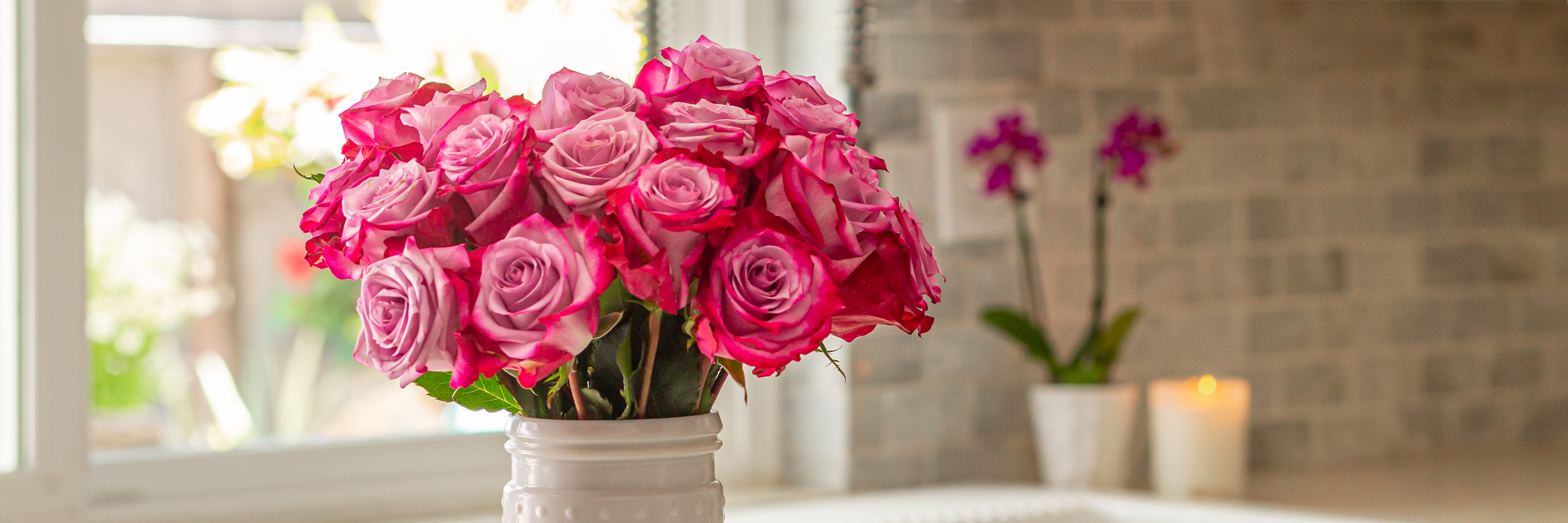 Vibrant pink roses elegantly arranged in a white vase, set against a cozy kitchen backdrop.