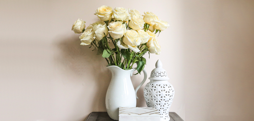 Elegant white roses in a vase beside a decorative jar and a chic box on a minimalist table.