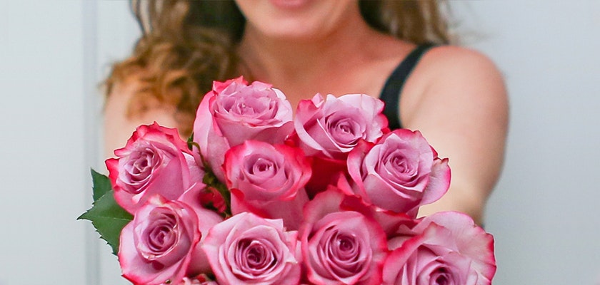 A beautiful bouquet of pink and lavender roses held by a smiling woman, ideal for gifting.