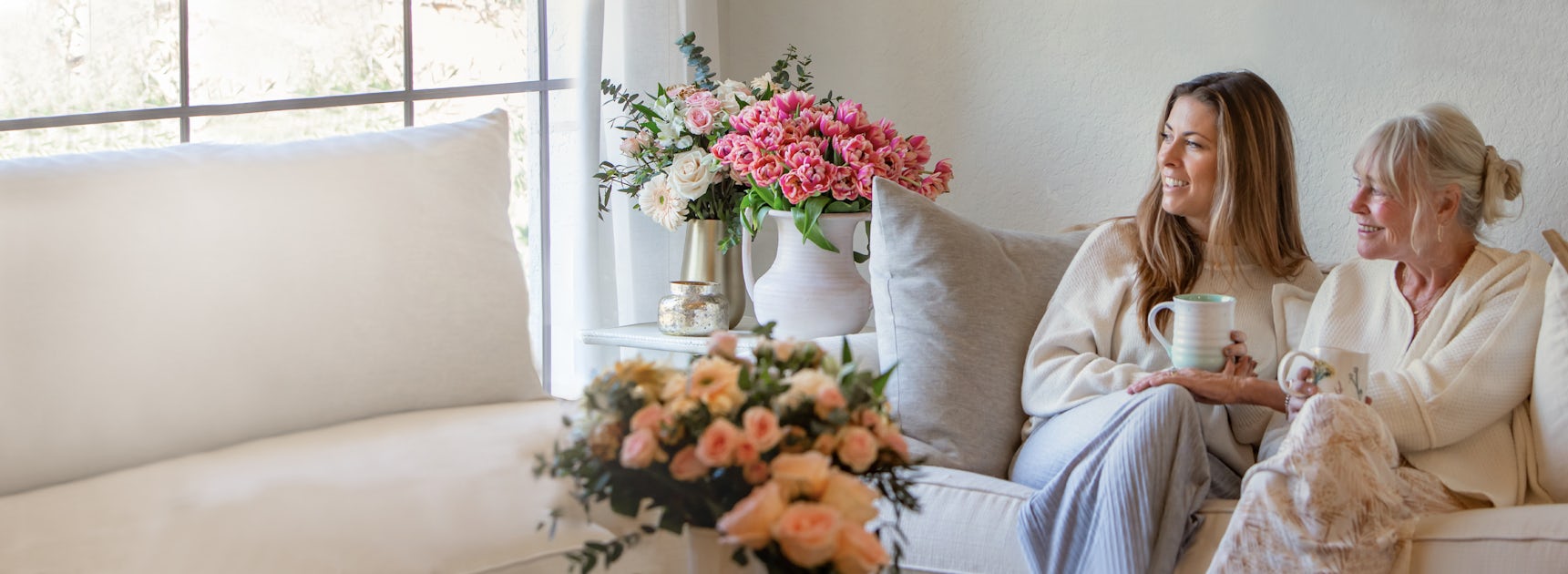 Two women enjoying a cozy moment together on a sofa, surrounded by beautiful flower arrangements.