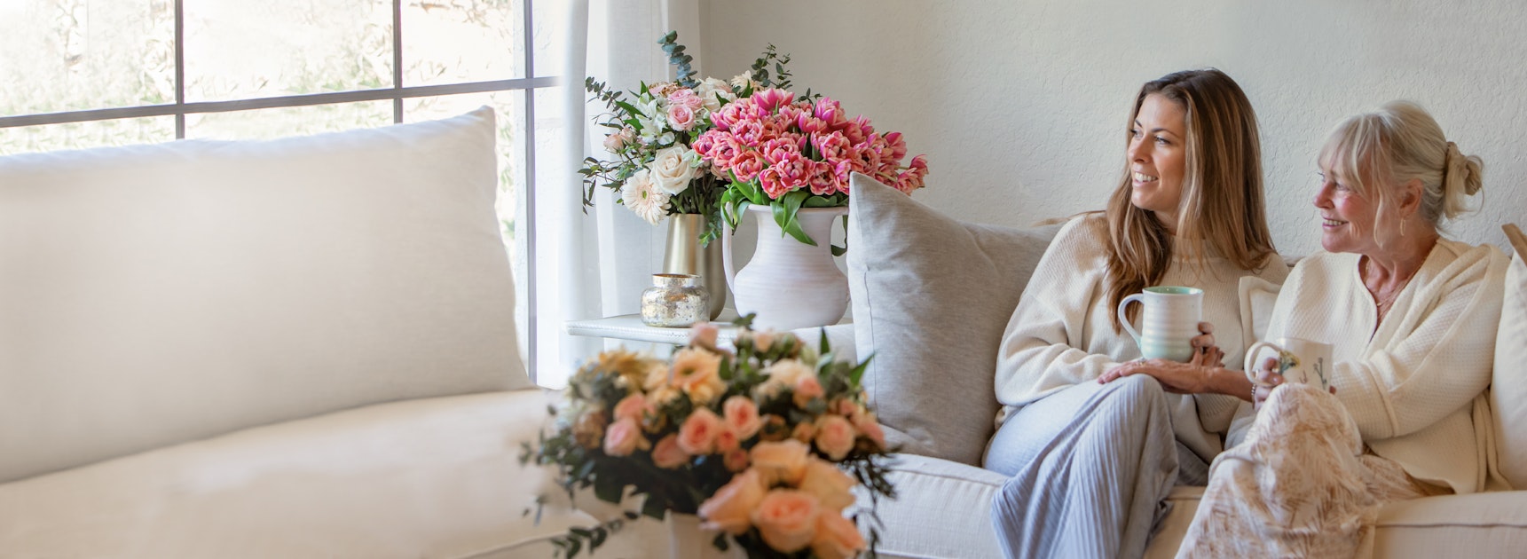 Two women enjoying a cozy moment together on a sofa, surrounded by beautiful flower arrangements.