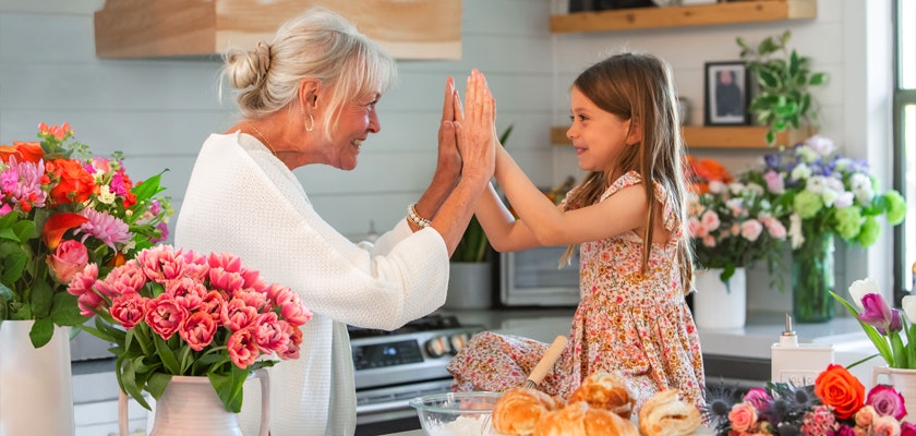 A warm, joyful moment between a grandmother and granddaughter in a floral-filled kitchen.
