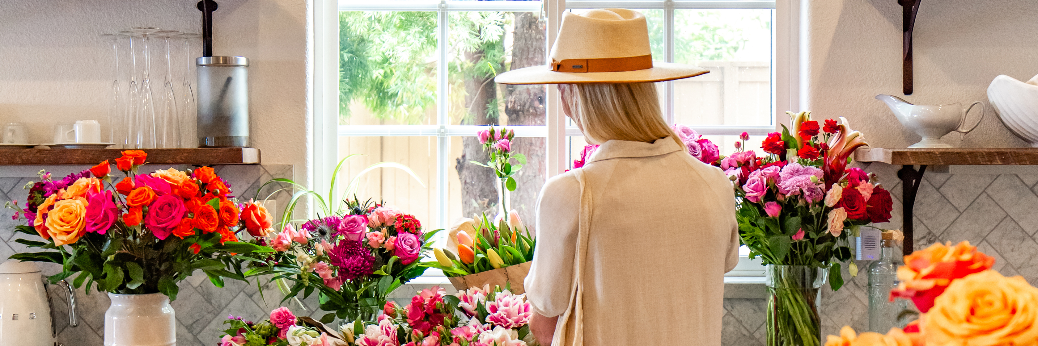 A woman in a stylish hat arranges colorful floral bouquets in a bright, inviting shop setting.
