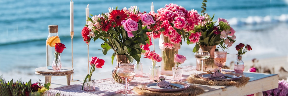 Elegant beachside table set with vibrant floral arrangements, candles, and charming decor.