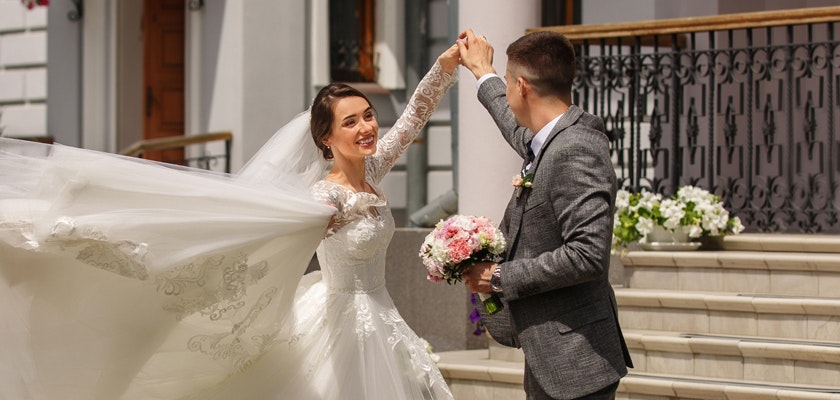 A joyful bride and groom dance together outside, capturing a romantic wedding moment with flowers.