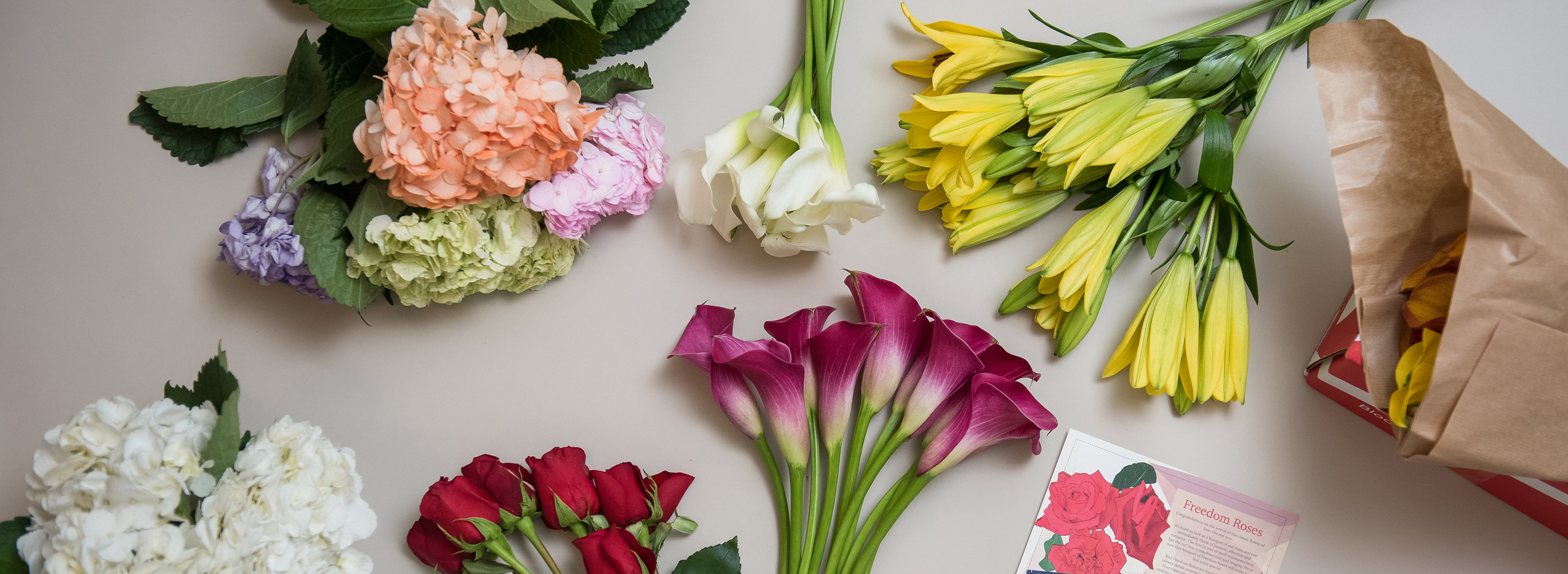 Colorful floral arrangement featuring roses, lilies, and hydrangeas on a light background.