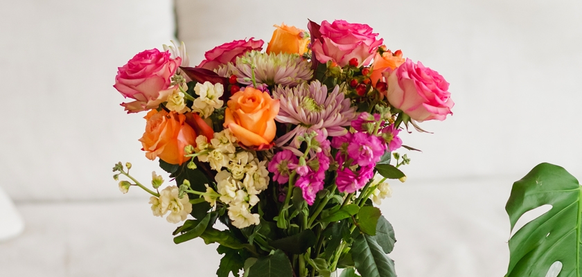 Vibrant floral arrangement with pink, orange roses and mixed seasonal blooms in lush greenery.