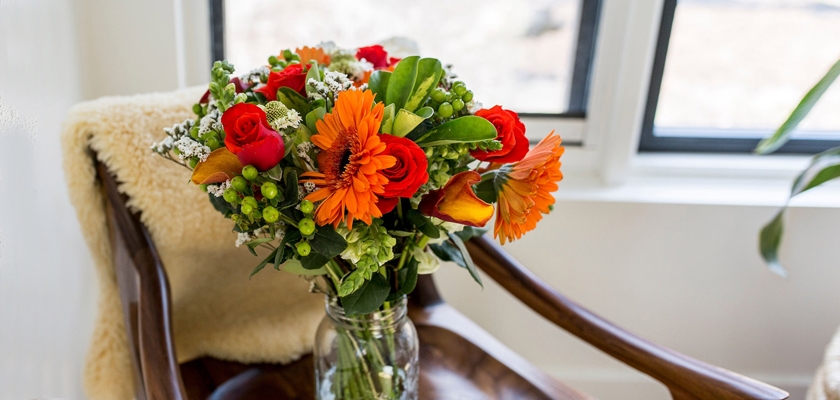 Vibrant floral arrangement featuring red roses, orange gerberas, and lush greenery in a vase.