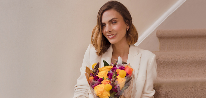 A stylish woman sitting on stairs, holding a vibrant floral bouquet with colorful blooms.