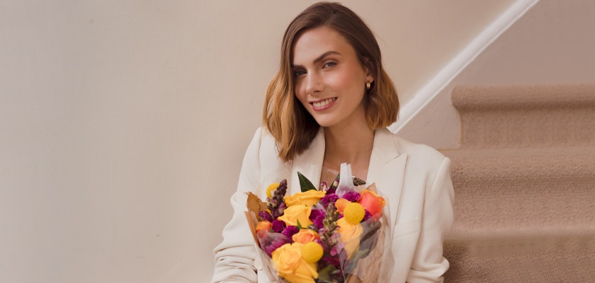 A stylish woman sitting on stairs, holding a vibrant floral bouquet with colorful blooms.