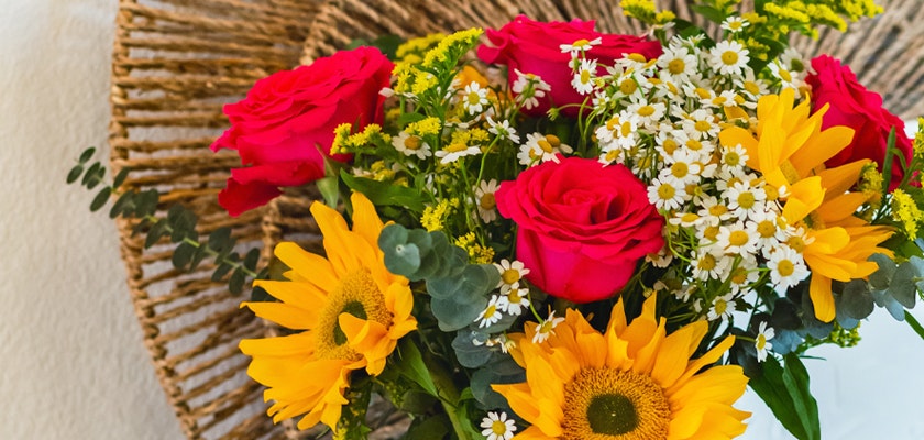 Vibrant bouquet featuring red roses, sunflowers, and delicate white flowers in a rustic setting.