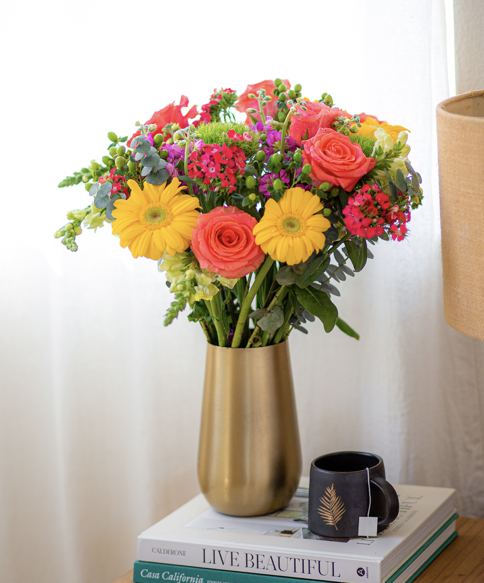 Vibrant bouquet featuring yellow gerberas, pink roses, and lush greenery in a chic vase.