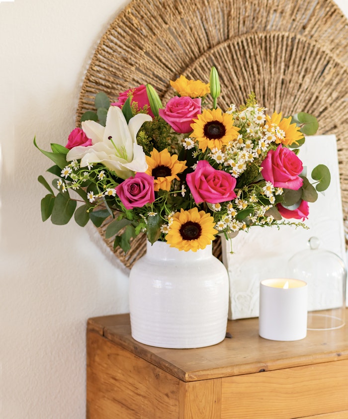 Vibrant floral arrangement featuring pink roses, sunflowers, and lilies in a stylish white vase.