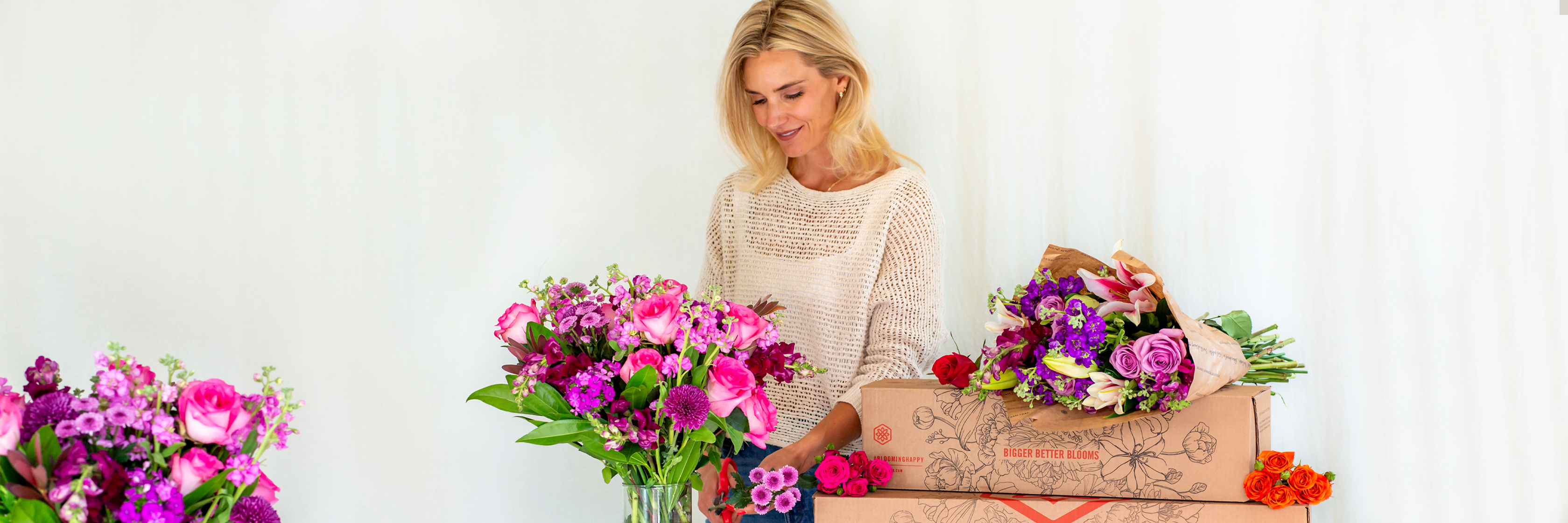 A woman arranging vibrant floral bouquets surrounded by colorful blooms in beautiful packaging.