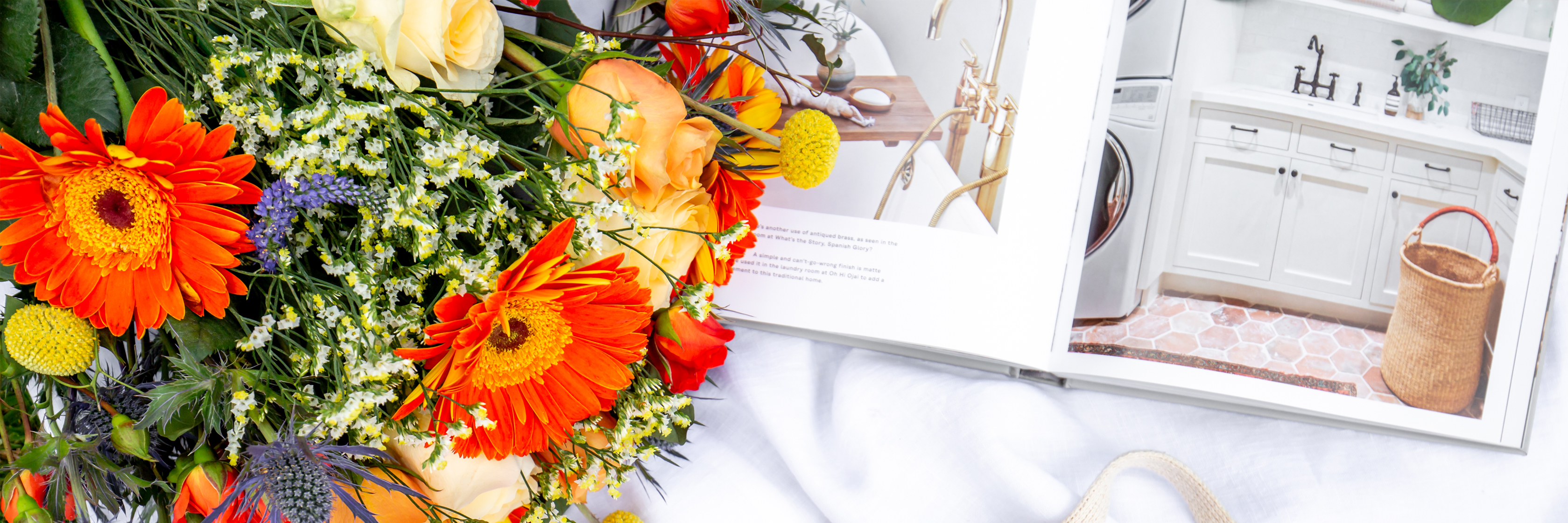Vibrant floral bouquet featuring orange gerberas and yellow roses beside a stylish home decor book.