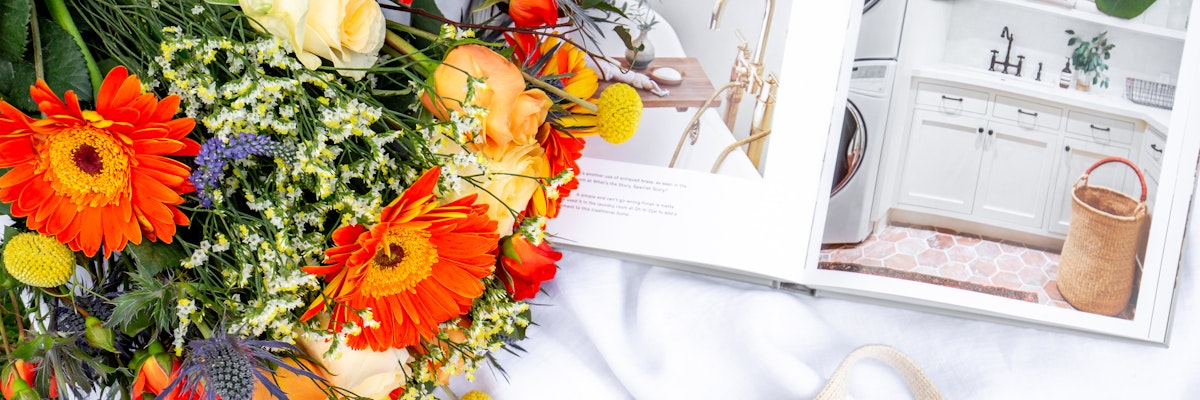 Vibrant floral bouquet featuring orange gerberas and yellow roses beside a stylish home decor book.